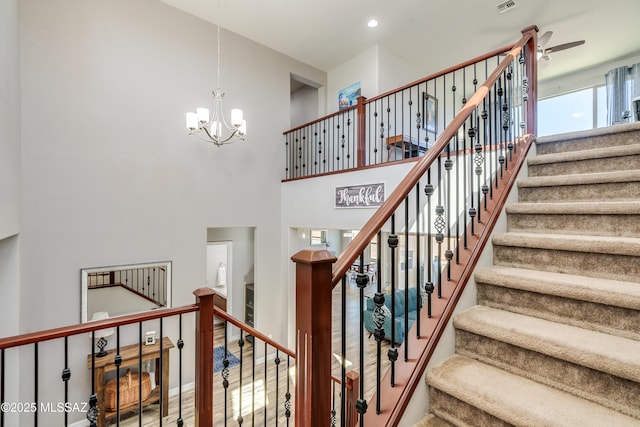 staircase featuring visible vents, a towering ceiling, and ceiling fan with notable chandelier