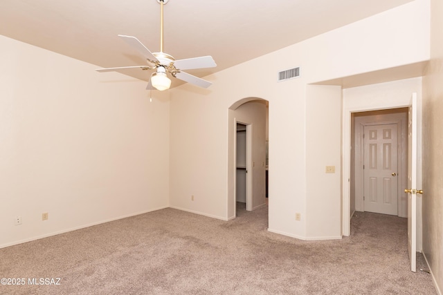 carpeted empty room with arched walkways, baseboards, ceiling fan, and visible vents