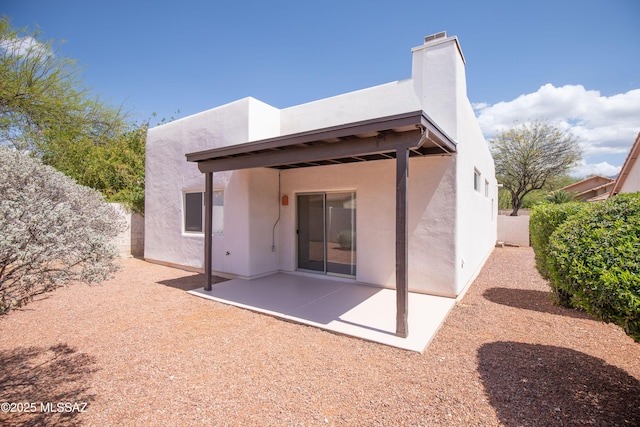 back of house featuring a chimney, stucco siding, fence, and a patio