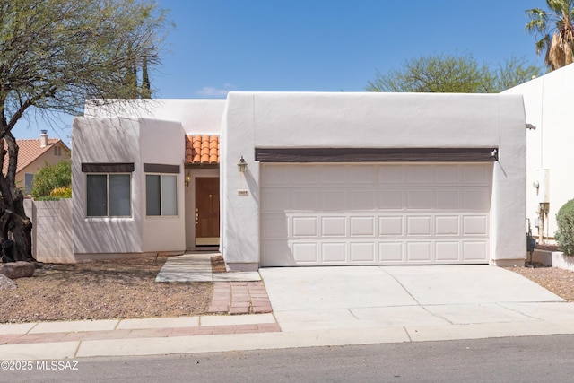 pueblo revival-style home with driveway, stucco siding, and an attached garage