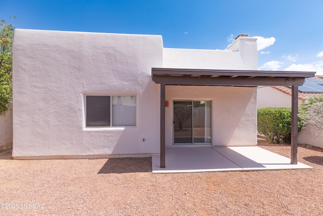 rear view of property with a chimney, stucco siding, and a patio area