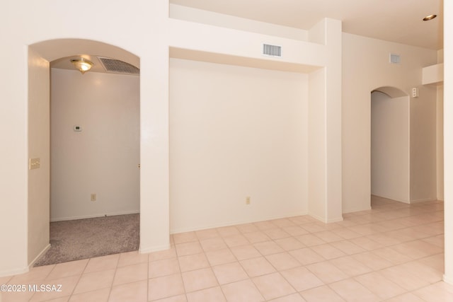 unfurnished room with arched walkways, visible vents, light tile patterned floors, and light carpet