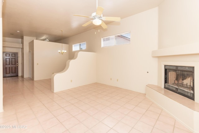 unfurnished living room featuring a tiled fireplace, light tile patterned floors, and ceiling fan with notable chandelier