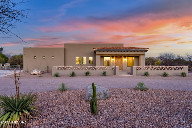 pueblo-style home with a tiled roof, a fenced front yard, covered porch, and stucco siding