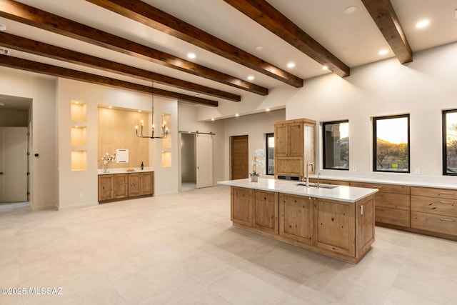 kitchen featuring beamed ceiling, a center island with sink, light countertops, a barn door, and a sink
