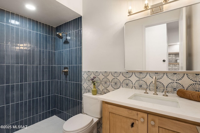 full bathroom featuring a tile shower, vanity, toilet, a wainscoted wall, and tile walls