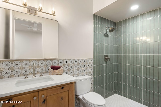 bathroom with wainscoting, vanity, toilet, tile walls, and tiled shower