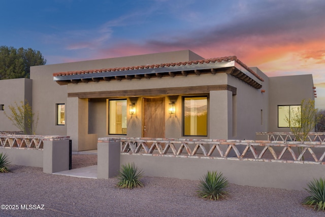 view of front facade with stucco siding, a tiled roof, and fence