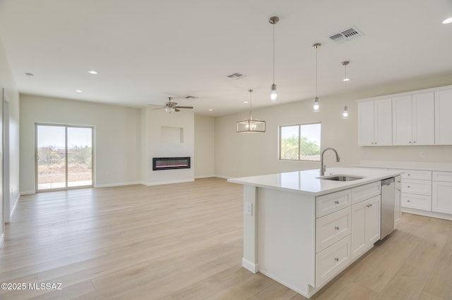 kitchen featuring stainless steel dishwasher, a sink, light wood-style floors, and a healthy amount of sunlight
