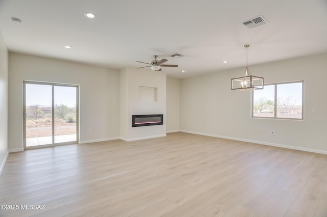 unfurnished living room featuring visible vents, recessed lighting, light wood finished floors, and a glass covered fireplace