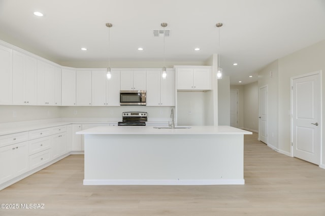 kitchen featuring visible vents, a kitchen island with sink, a sink, light wood-style flooring, and stainless steel appliances