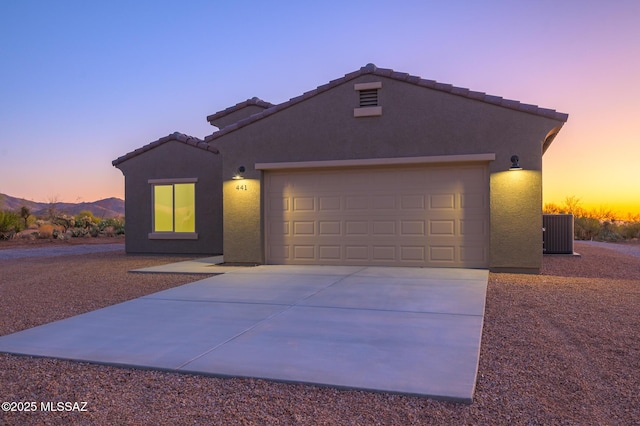 view of front facade featuring a garage, stucco siding, central air condition unit, a tiled roof, and driveway