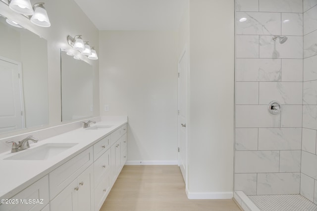 full bath with double vanity, tiled shower, a sink, and wood finished floors