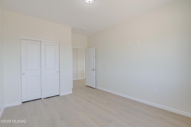 unfurnished bedroom featuring light wood-style floors, baseboards, and a closet