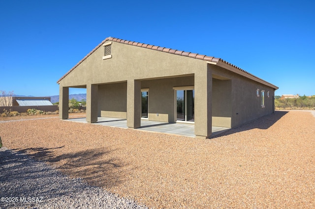 back of property with stucco siding, a patio area, and a tile roof
