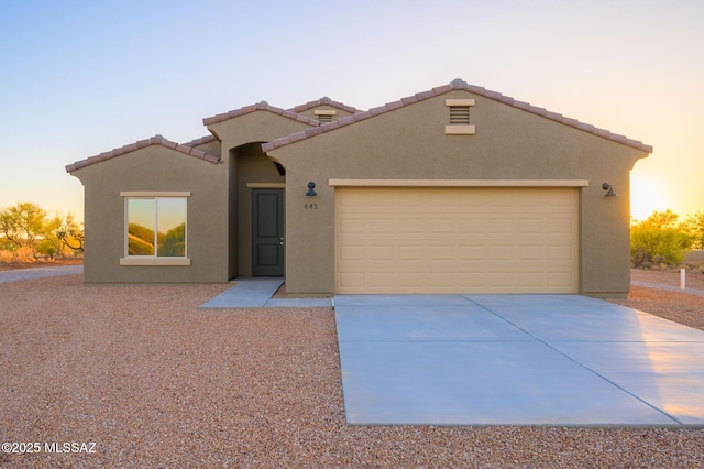 view of front facade with a tiled roof, an attached garage, stucco siding, and driveway