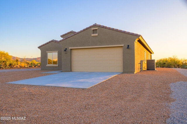 view of front facade with stucco siding, an attached garage, central air condition unit, and driveway