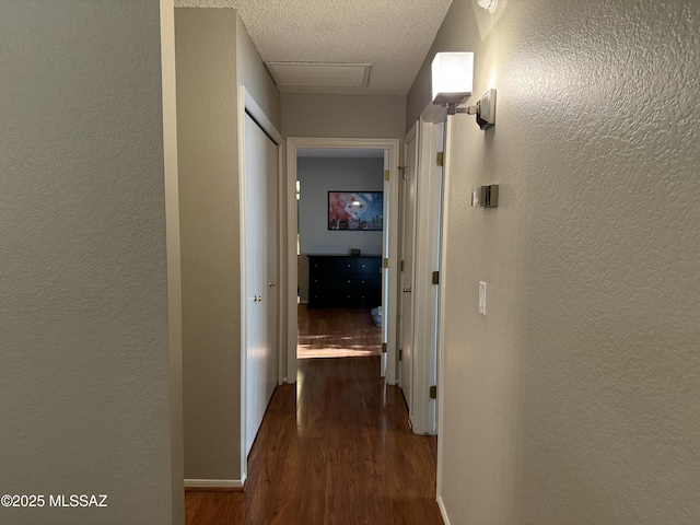 hallway with a textured wall, baseboards, attic access, and wood finished floors