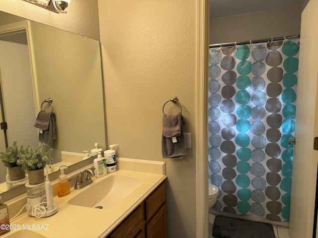 full bathroom with toilet, curtained shower, a textured wall, and vanity