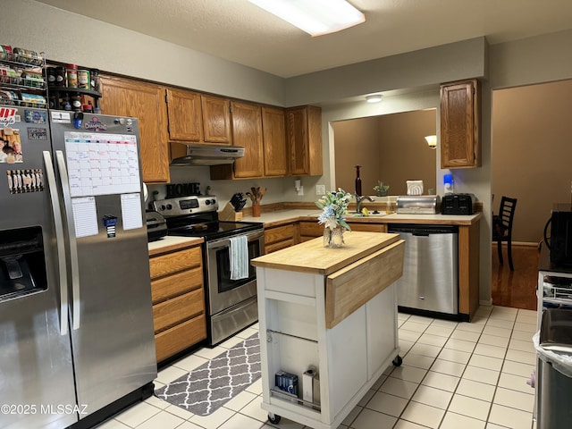 kitchen featuring under cabinet range hood, wood counters, light tile patterned floors, and stainless steel appliances