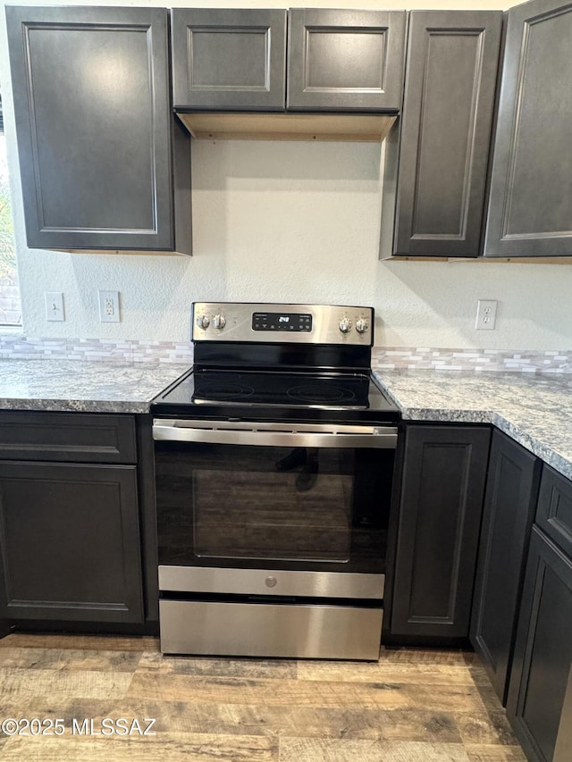 kitchen with stainless steel electric stove, light stone counters, and light wood-style flooring