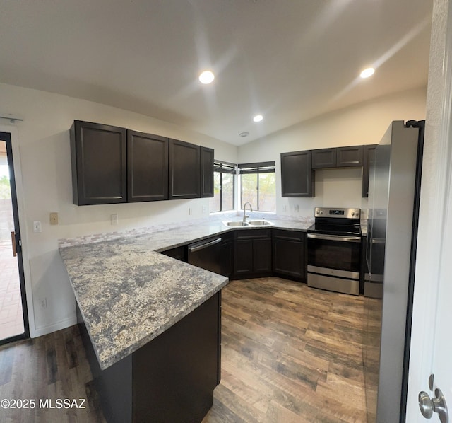 kitchen featuring dark wood-style flooring, appliances with stainless steel finishes, a sink, a peninsula, and lofted ceiling