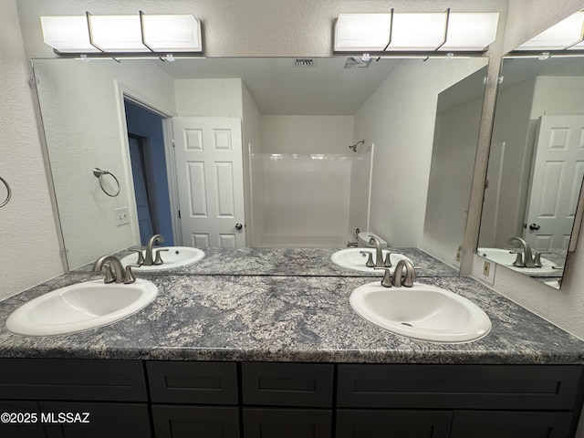 bathroom featuring a sink, a textured wall, and double vanity