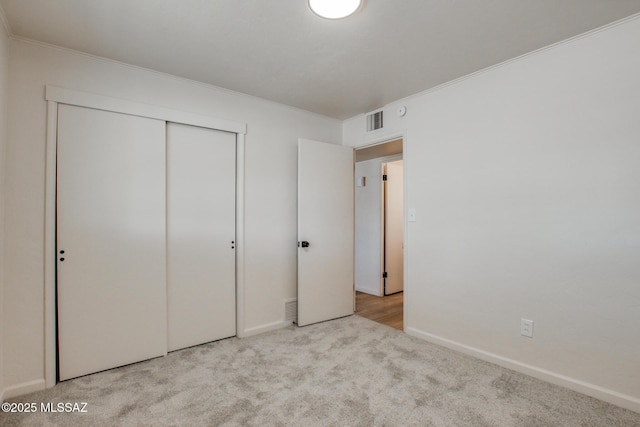 unfurnished bedroom with a closet, carpet flooring, visible vents, baseboards, and ornamental molding