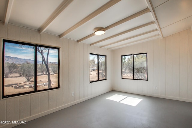 unfurnished room featuring a healthy amount of sunlight, concrete floors, and beamed ceiling