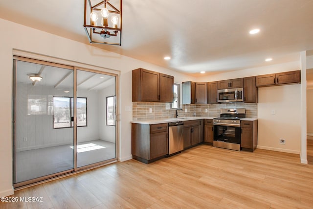 kitchen with light countertops, a sink, light wood-style flooring, stainless steel appliances, and decorative backsplash