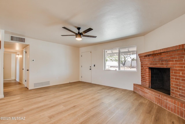 unfurnished living room with visible vents, wood finished floors, ceiling fan, and a brick fireplace