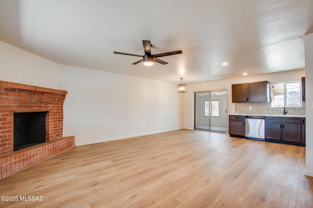 unfurnished living room with light wood-type flooring, baseboards, a sink, ceiling fan, and a brick fireplace