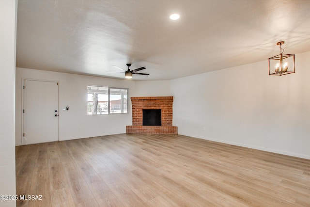unfurnished living room featuring a brick fireplace, ceiling fan with notable chandelier, light wood-style floors, and baseboards