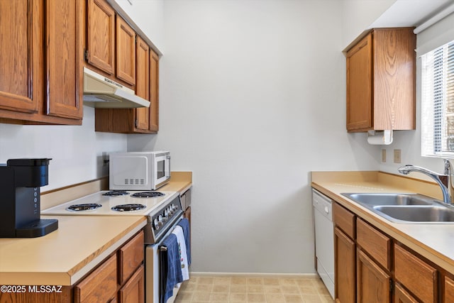 kitchen featuring white appliances, light countertops, under cabinet range hood, brown cabinetry, and a sink