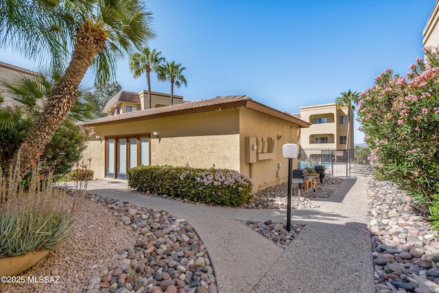 view of side of home with a tiled roof, stucco siding, and a gate