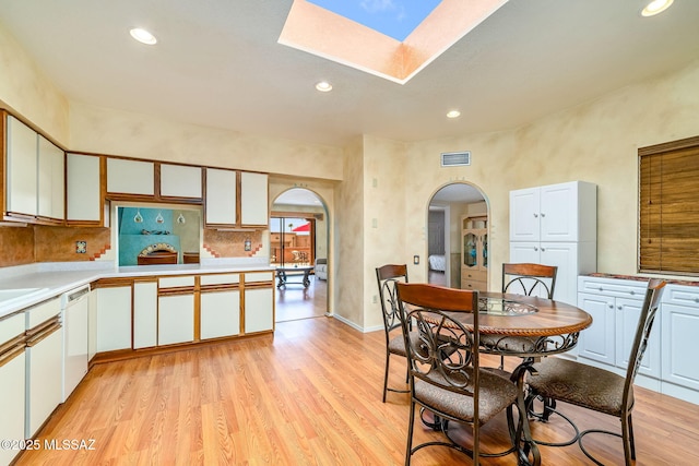 dining space featuring light wood finished floors, a skylight, visible vents, arched walkways, and recessed lighting