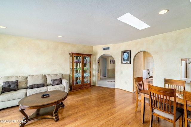 living area featuring a skylight, light wood-style flooring, visible vents, arched walkways, and recessed lighting