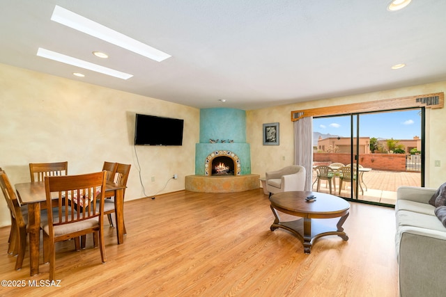 living area featuring a fireplace, light wood-style flooring, recessed lighting, and a skylight