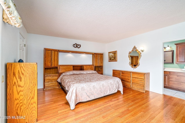 bedroom featuring ensuite bathroom, light wood finished floors, and a textured ceiling