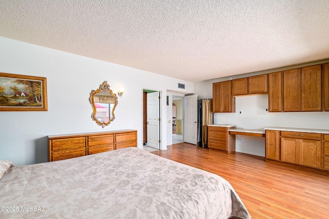 bedroom with light wood finished floors, visible vents, and a textured ceiling