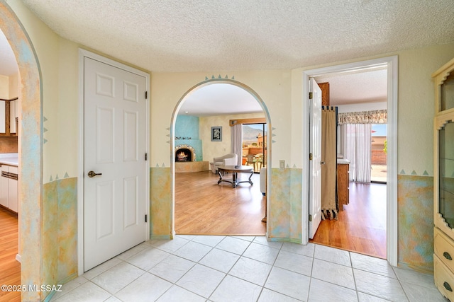 hall with arched walkways, a textured ceiling, and light tile patterned floors