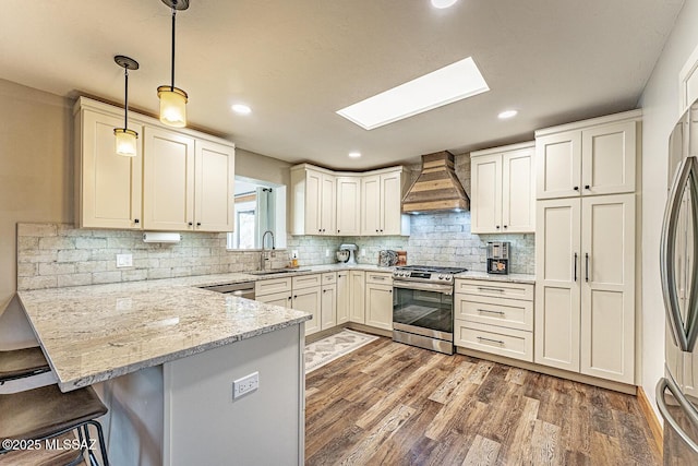 kitchen featuring a kitchen bar, stainless steel appliances, a sink, a peninsula, and custom exhaust hood