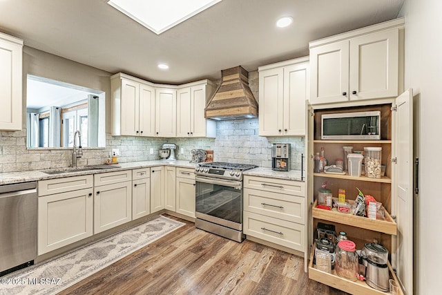 kitchen featuring decorative backsplash, custom exhaust hood, stainless steel appliances, a sink, and light wood-type flooring