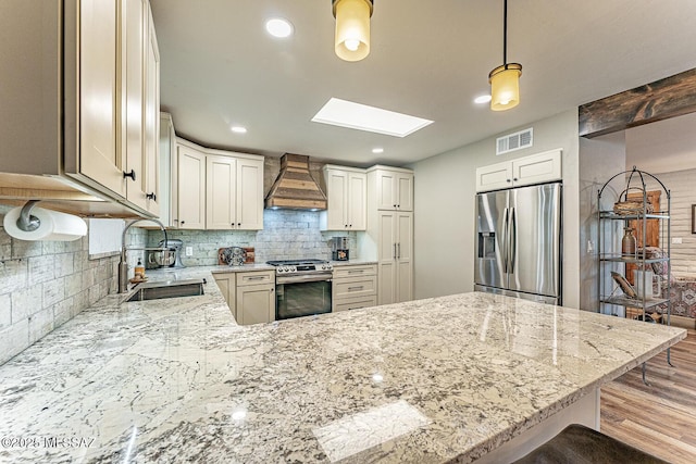 kitchen with visible vents, a skylight, stainless steel appliances, premium range hood, and a sink
