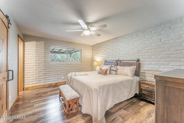 bedroom with baseboards, a textured ceiling, brick wall, ceiling fan, and wood finished floors