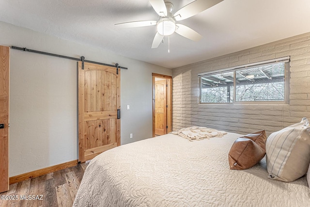bedroom featuring baseboards, a barn door, wood finished floors, and brick wall