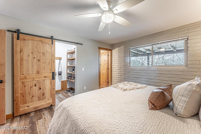 bedroom featuring a barn door, wood finished floors, and brick wall