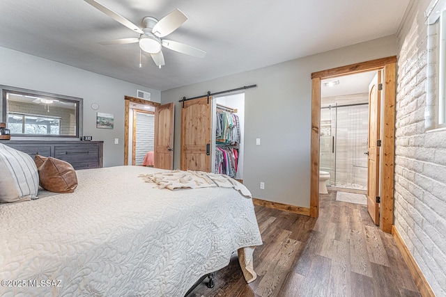 bedroom featuring baseboards, wood finished floors, a barn door, ensuite bath, and a spacious closet
