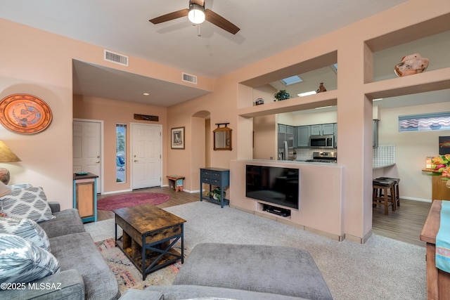 living room with arched walkways, visible vents, baseboards, and ceiling fan