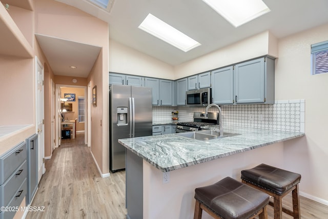 kitchen with a peninsula, appliances with stainless steel finishes, light stone counters, a sink, and backsplash